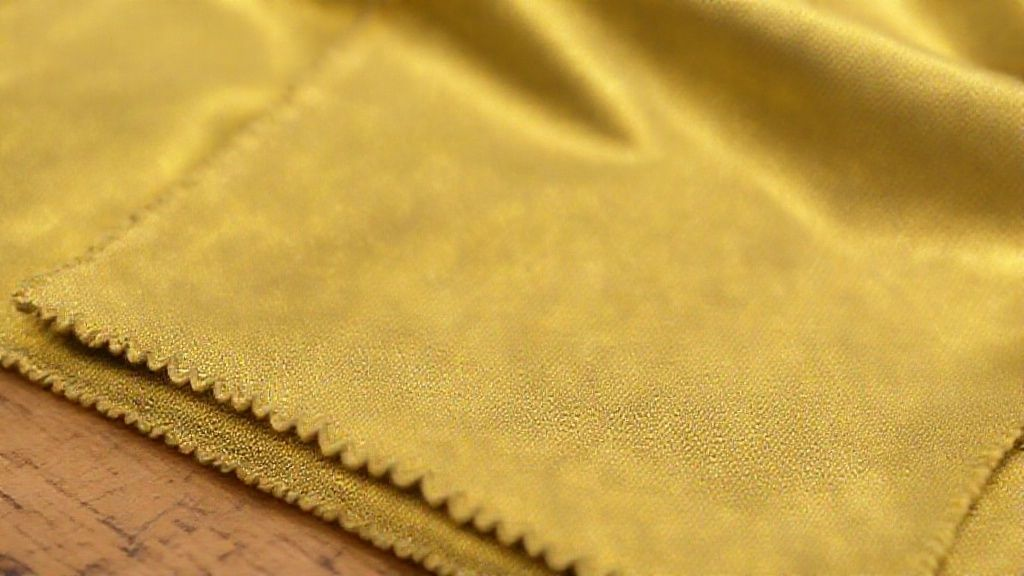 A hand gently cleaning a gold anodized titanium ring with a soft cloth and mild soap.