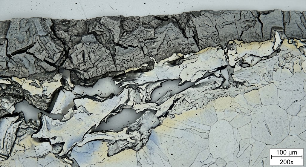 Cross-section optical metallography micrograph at 200x magnification illustrating the brittle alpha-case layer on titanium versus peeled base metal